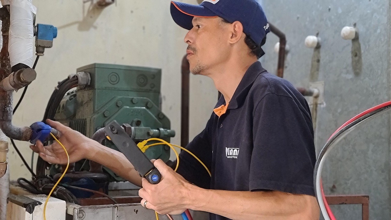 AC technician using refrigerant gauges on an outdoor compressor unit